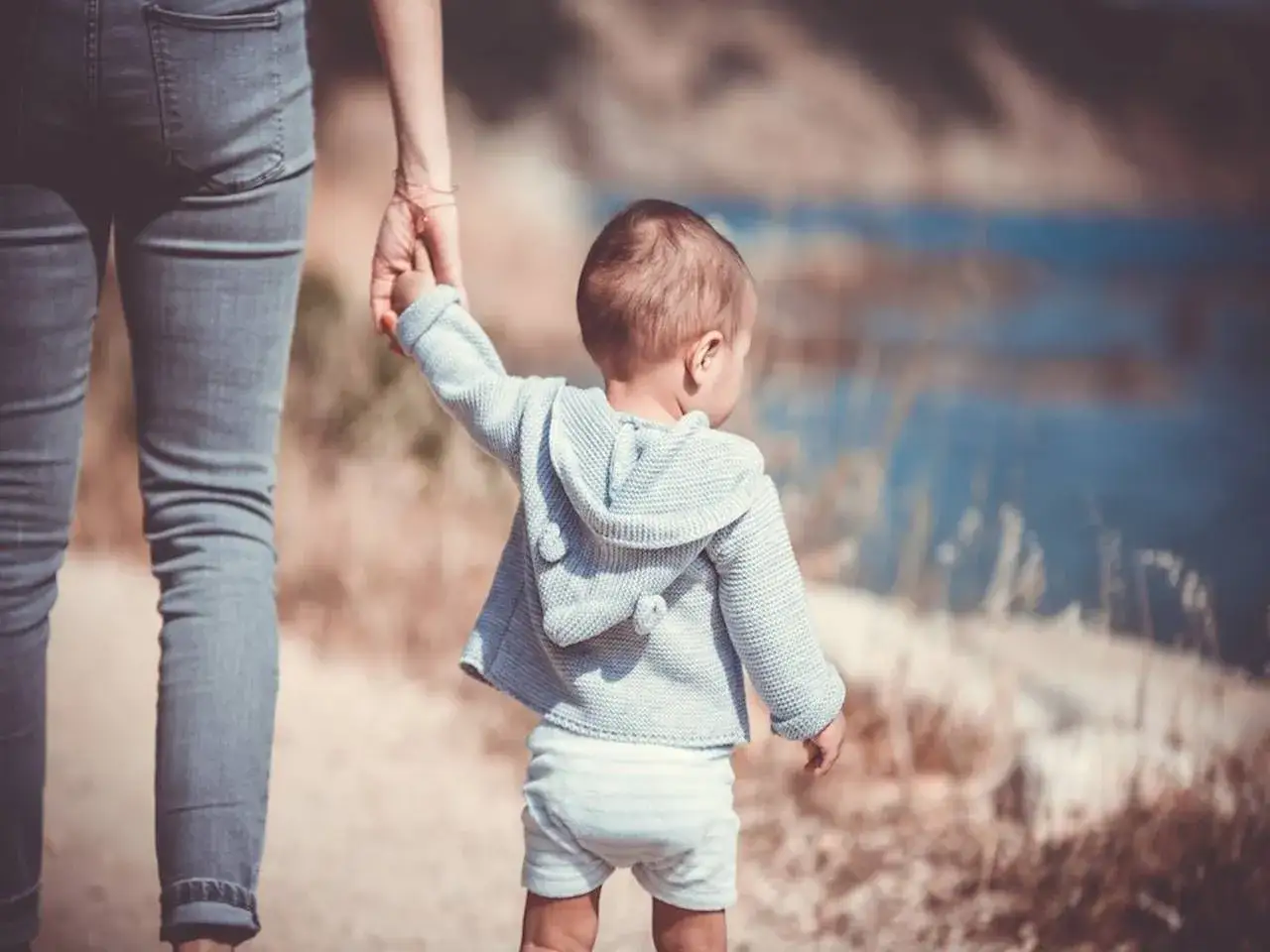 Dziecko z lękiem separacyjnym trzyma się ręki mamy, idąc ścieżką przy wodzie.
